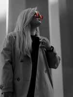 femme dans une bronzer tranchée manteau avec une noir chemise et rouge des lunettes de soleil dans le ville photo
