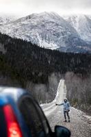 Femme faisant de l'auto-stop sur une route d'hiver avec de belles montagnes enneigées en arrière-plan photo