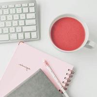 espace de travail blanc avec carnet de notes rose clair et fleur blanche avec café sur table blanche. photo