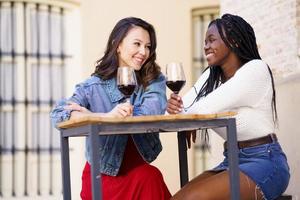 deux femmes buvant du vin rouge assises à une table devant un bar.