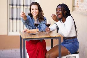 deux femmes buvant du vin rouge assises à une table devant un bar. photo