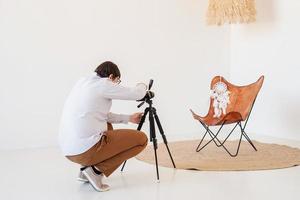 photographe masculin travaillant dans un intérieur léger et aéré, chaise blanche et beige, tapis photo