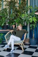 Jeune femme blonde assise sur une chaise confortable entourée de plantes photo