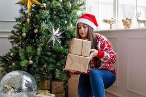 Jeune femme en pull rouge tenant une pile de cadeaux de Noël photo