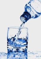 Résumé d'éclaboussure de verre de bouteille transparente d'eau bleue avec des bulles sur le blanc. photo