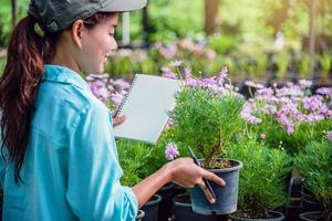 jeune femme heureuse travaillant dans une serre, écrivant des notes et étudiant la croissance des arbres. photo