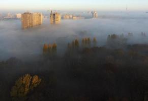 les rayons du soleil illuminent la ville du matin à travers le brouillard dense d'automne photo
