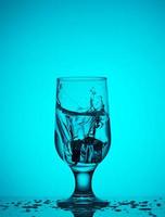 un glaçon tombe dans un verre en verre avec de l'eau photo