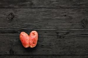 pomme de terre laide en forme de coeur sur un fond en bois noir. concept de gaspillage de légumes ou de nourriture. vue de dessus, gros plan. photo
