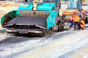 un grand finisseur d'asphalte et un rouleau vibrant routier se succèdent pour la construction d'une nouvelle route asphaltée. photo