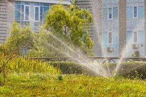 les jets d'eau d'un pulvérisateur de jardin irriguent la pelouse dans la chaleur estivale de la journée. photo