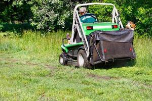 un employé des services publics s'occupe de la pelouse et tond l'herbe avec une tondeuse à gazon. photo