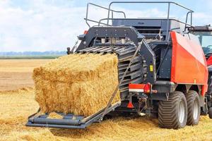 un tracteur agricole avec une unité traînée transforme des balles de paille en briquettes denses dans un champ de blé.