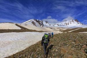 un groupe de touristes escalade la pente rocheuse de la montagne jusqu'au sommet enneigé photo