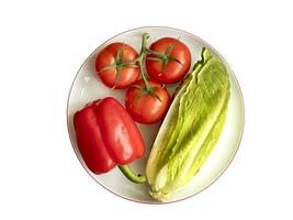 Le poivre bulgare, la branche de tomate et la laitue romaine se trouvent en gros plan sur une assiette en porcelaine ronde blanche avec un rebord en grenade photo