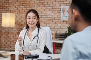 belle femme médecin en chemise blanche qui est une personne asiatique avec stéthoscope examine la santé d'un patient masculin dans une clinique médicale sur fond de mur de briques, souriant conseillant une profession de spécialiste médical. photo