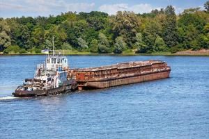 un remorqueur fluvial avec une barge rouillée vide traverse une large rivière. photo