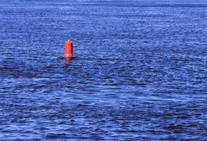 une bouée rouge flotte sur les vagues bleues d'une large rivière. photo