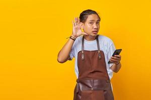 portrait d'un barista sérieux essayant d'entendre une conversation secrète et tenant un smartphone photo