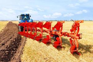 tracteur agricole couplé à une charrue métallique sur un champ de blé récolté. photo