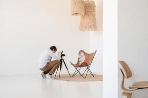 photographe masculin travaillant dans un intérieur minimal léger et aéré, chaise, tapis et oreillers blancs et beiges photo