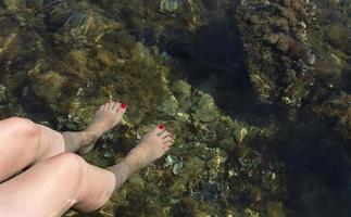 les jambes féminines avec une pédicure rouge sont descendues dans les eaux marines transparentes de la mer adriatique photo