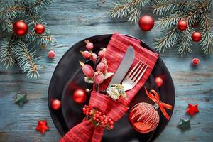mise à plat avec des décorations de Noël en vert et rouge avec des baies givrées, des bibelots, des assiettes et de la vaisselle