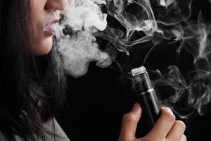 Close up young woman smoking e-cigarette sur fond noir photo