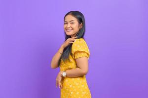souriante jeune femme asiatique vêtue d'une robe jaune et ayant l'air confiante sur fond violet photo