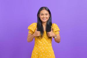 Portrait de jeune femme asiatique souriante montrant les pouces vers le haut à la caméra sur fond violet photo