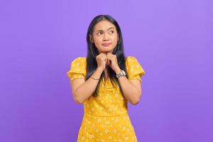 jolie jeune femme asiatique garde la main sous le menton et regarde de côté isolé sur fond violet photo