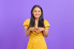 souriante jeune femme asiatique garde la main ensemble et se sent optimiste sur fond violet