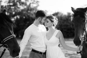 fille dans une robe d'été blanche et un gars dans une chemise blanche sur une promenade avec des chevaux bruns photo