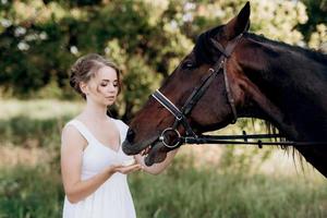 fille dans une robe d'été blanche sur une promenade avec des chevaux bruns photo