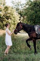 fille dans une robe d'été blanche sur une promenade avec des chevaux bruns photo