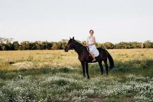 fille dans une robe d'été blanche sur une promenade avec des chevaux bruns photo