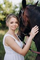 fille dans une robe d'été blanche sur une promenade avec des chevaux bruns photo