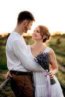 fille dans une robe d'été blanche et un gars dans une chemise blanche sur une promenade au coucher du soleil avec un bouquet photo