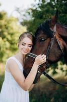 fille dans une robe d'été blanche sur une promenade avec des chevaux bruns photo