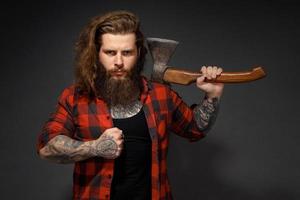 bel homme aux cheveux longs avec une hache dans les mains sur un fond de studio sombre photo