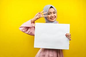 jolie jeune femme musulmane joyeuse tenant une bannière vide vierge, une pancarte, un tableau blanc, un panneau vierge, un panneau publicitaire blanc, présentant quelque chose dans l'espace de copie, promotion photo