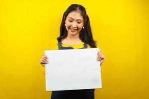 jolie et mignonne jeune femme joyeuse tenant une bannière vide vierge, une pancarte, un tableau blanc, un panneau vierge, un panneau publicitaire blanc, présentant quelque chose dans l'espace de copie, promotion photo