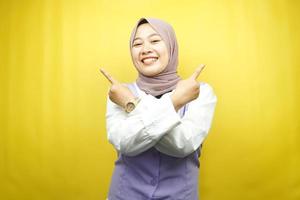 belle jeune femme musulmane asiatique souriante confiante, enthousiaste, joyeuse avec les mains pointant l'espace vide présentant quelque chose, regardant la caméra isolée sur fond jaune, concept publicitaire photo