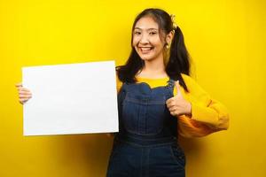 jolie et mignonne jeune femme joyeuse tenant une bannière vide vierge, une pancarte, un tableau blanc, un panneau vierge, un panneau publicitaire blanc, présentant quelque chose dans l'espace de copie, promotion photo