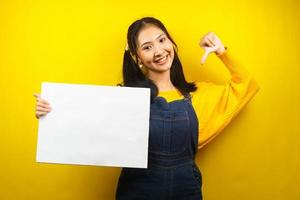 jolie et mignonne jeune femme joyeuse tenant une bannière vide vierge, une pancarte, un tableau blanc, un panneau vierge, un panneau publicitaire blanc, présentant quelque chose dans l'espace de copie, promotion photo