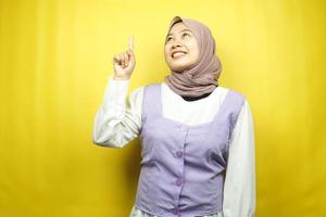 belle jeune femme musulmane asiatique souriante confiante, enthousiaste et joyeuse avec les mains pointées vers le haut, trouver des idées, proposer des solutions, présenter quelque chose, isolée sur fond jaune photo