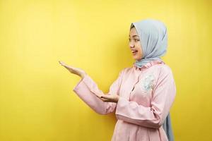 joyeuse belle jeune femme musulmane, la main pointant vers l'espace vide, faisant la promotion de quelque chose, isolée