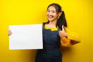 jolie et mignonne jeune femme joyeuse tenant une bannière vide vierge, une pancarte, un tableau blanc, un panneau vierge, un panneau publicitaire blanc, présentant quelque chose dans l'espace de copie, promotion photo