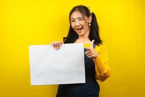 jolie et mignonne jeune femme joyeuse tenant une bannière vide vierge, une pancarte, un tableau blanc, un panneau vierge, un panneau publicitaire blanc, présentant quelque chose dans l'espace de copie, promotion photo