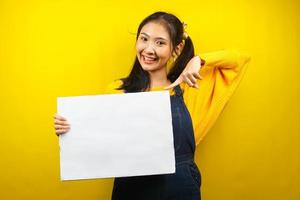 jolie et mignonne jeune femme joyeuse tenant une bannière vide vierge, une pancarte, un tableau blanc, un panneau vierge, un panneau publicitaire blanc, présentant quelque chose dans l'espace de copie, promotion photo